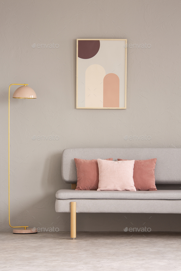 Pink lamp next to grey couch with cushions in living room interi